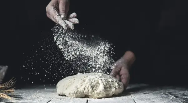 Händer strör mjöl över deg. Jämförelse mellan dinkelmjöl vs vetemjöl i bakning.