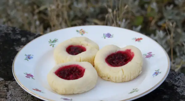 Tre glutenfria hallongrottor med sylt på en blommig tallrik.
