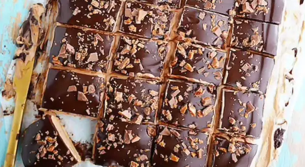 Biskvier i långpanna med chokladglasyr och krossad toffee. En gyllene kniv ligger bredvid.