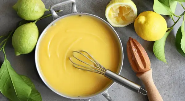 Kastrull med krämig lemon curd, färska citroner och en träpress. Perfekt för bakning!