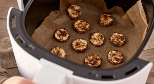 Små, runda kakor med kanel ligger på bakplåtspapper i en airfryer. Perfekt för att frysa in kakor för senare njutning.