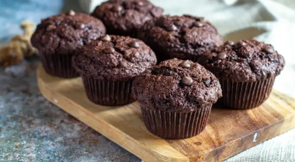 Fem amerikanska muffins med chokladbitar på en träbricka.