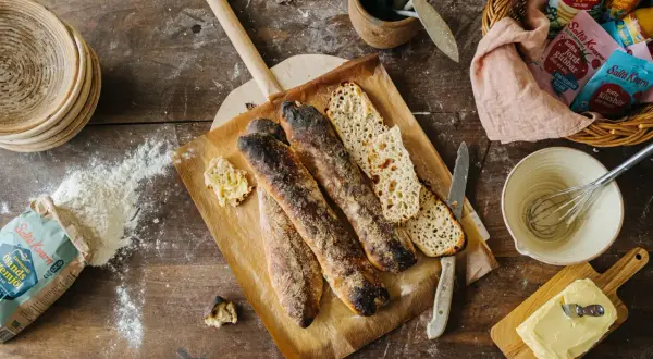 Nybakade surdegsbröd på en bakplåt, redo för ett gott surdeg recept. Ingredienser som mjöl och smör ligger utspridda.