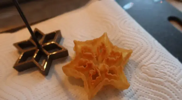 En stjärnformad struva, nyligen friterad, ligger på hushållspapper bredvid sin form. Ett perfekt resultat för struvor recept.
