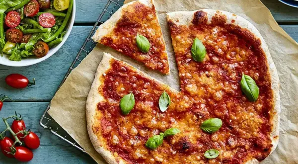 En hemmagjord pizza med nyttig pizzabotten, toppad med tomatsås och basilika. Bredvid en fräsch sallad med gröna bönor och tomater.