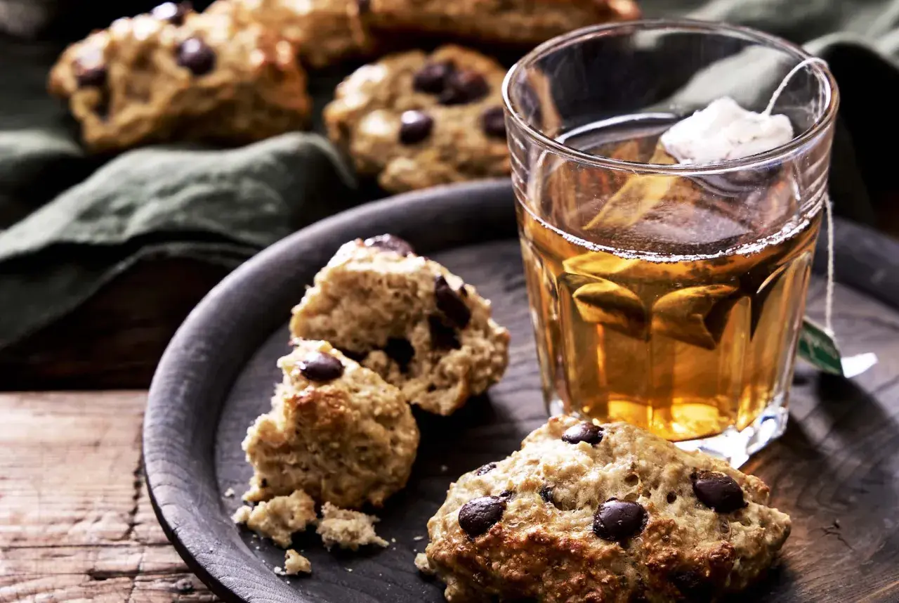 Nyttigare scones med chokladbitar på en mörk bricka bredvid ett glas te. Perfekt fika!