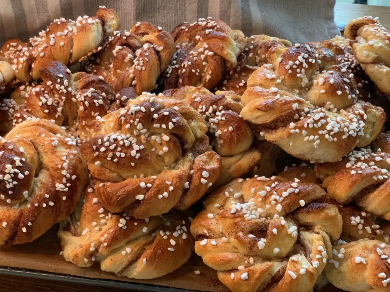 En hög med nybakade kanelbullar, perfekta att baka med flytande margarin. Strösslade med pärlsocker.