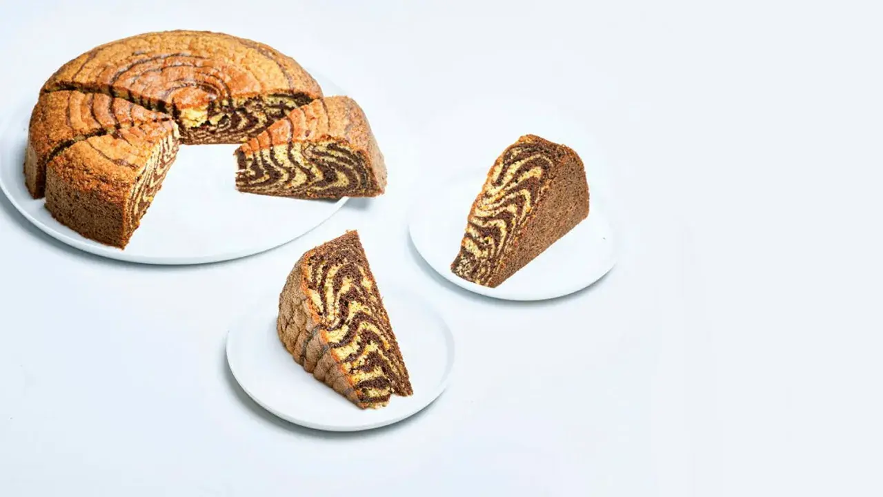 A sliced zebra cake with a marbled chocolate and vanilla pattern, served on white plates.