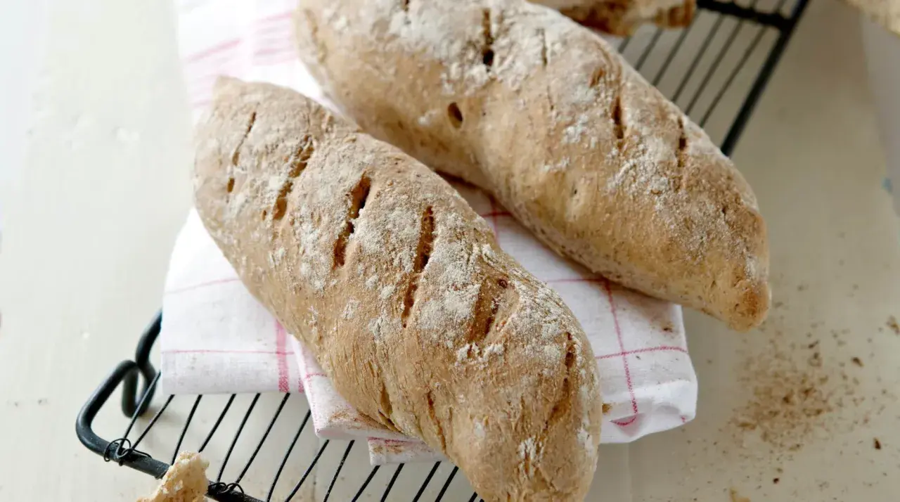 Två nybakade bröd, perfekta för ett skrädmjöl recept. Ligger på ett rutigt tyg på ett galler.