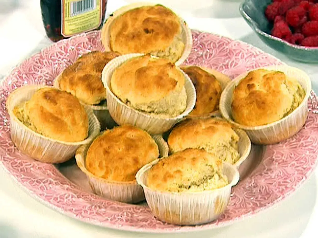 En rosa bricka med nybakade dinkelscones i pappersformar. Bredvid syns hallon och en burk sylt.