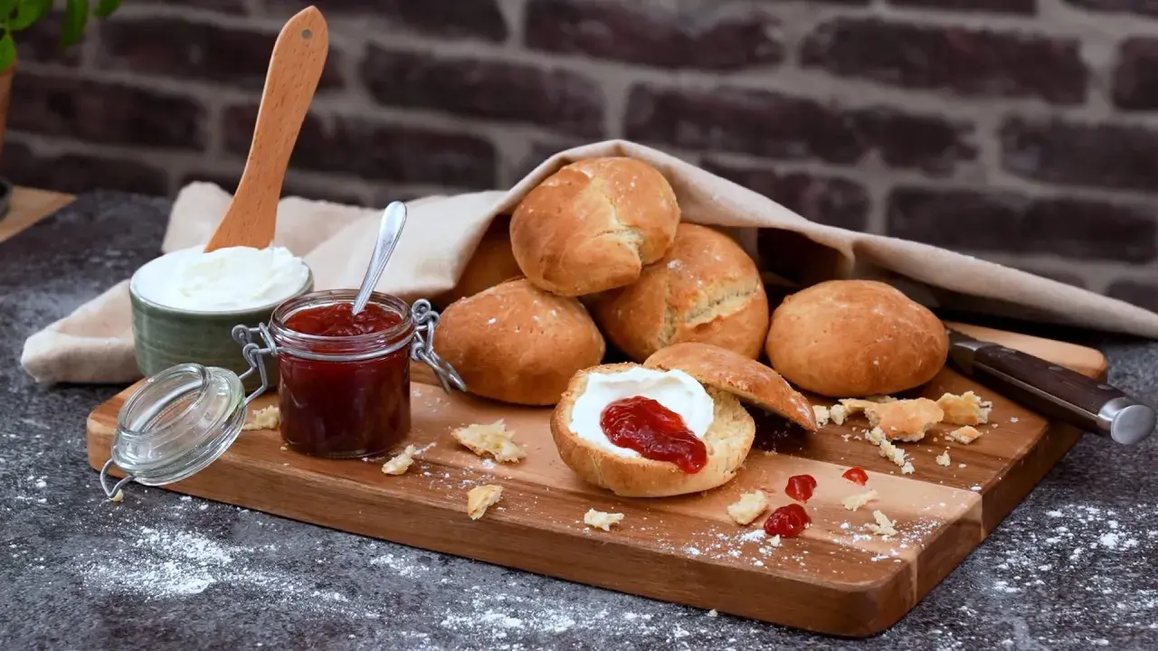 Färska scones havregryn med sylt och grädde på en träskärbräda.