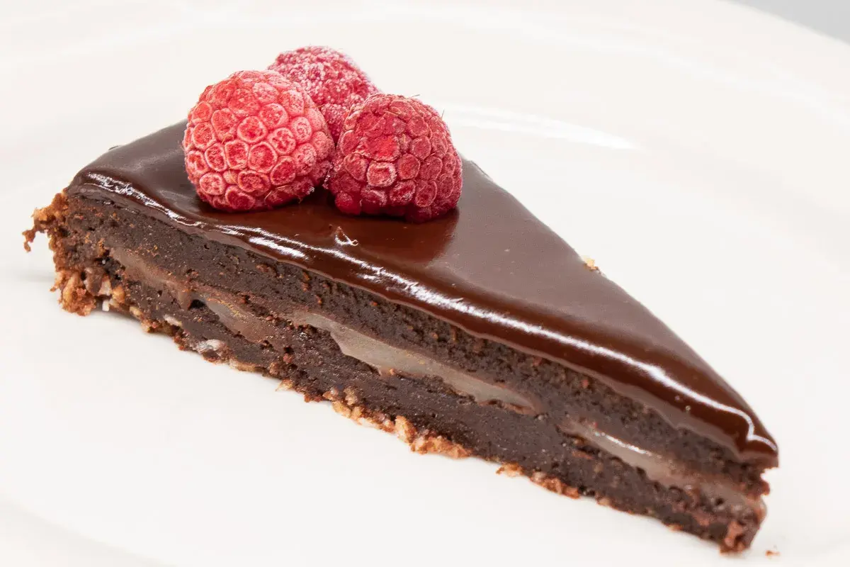 En bit kladdkaka med After Eight-smak, toppad med tre hallon på en vit tallrik.