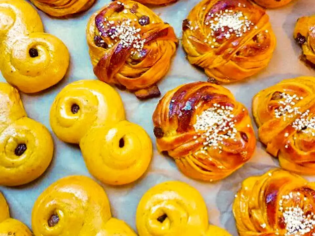 En närbild av saftiga lussebullar, vissa med russin och pärlsocker, andra med enbart russin. De ser otroligt goda ut!