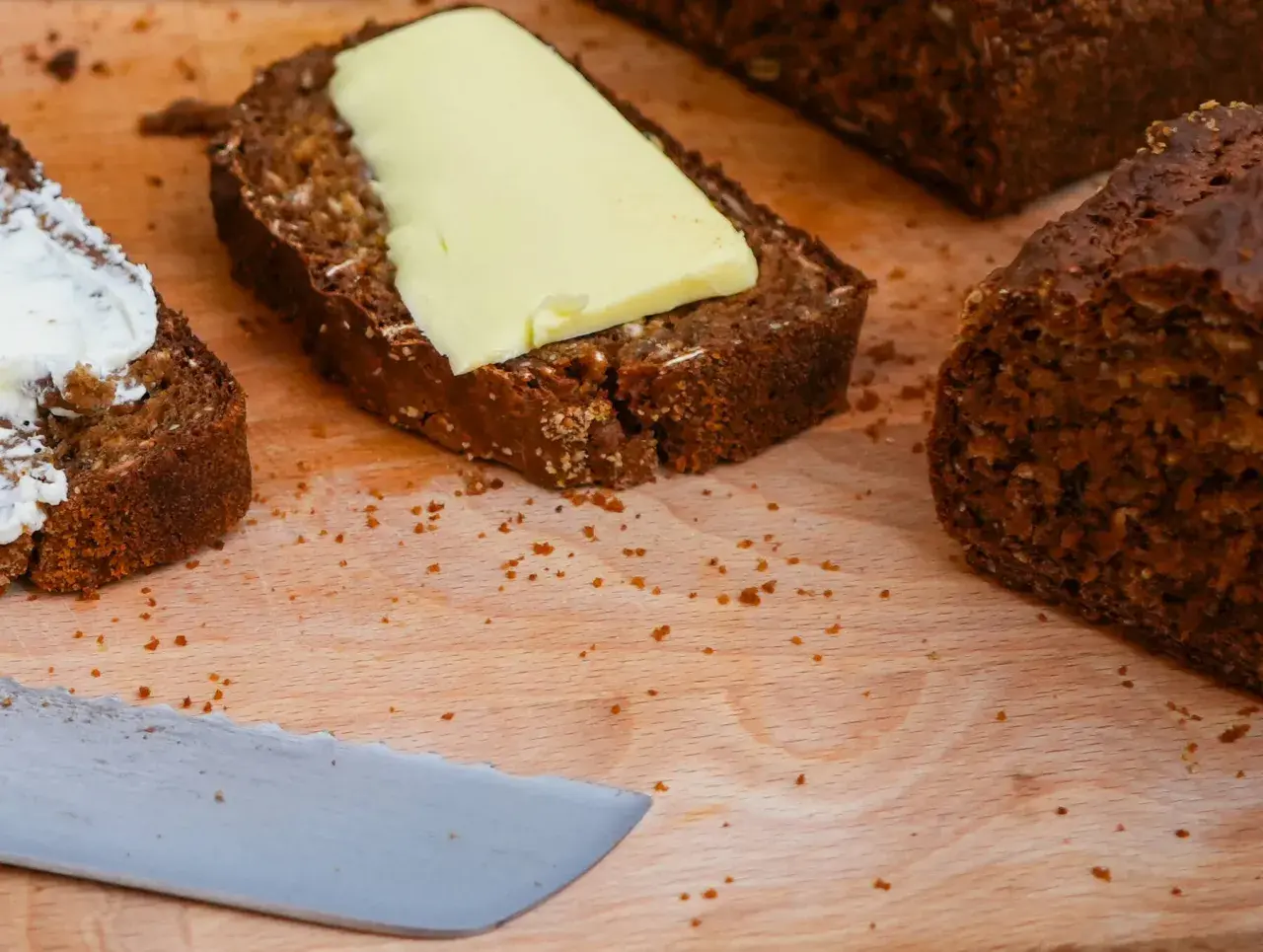 Mörkt bröd med smör och en skiva med yoghurt på en skärbräda.