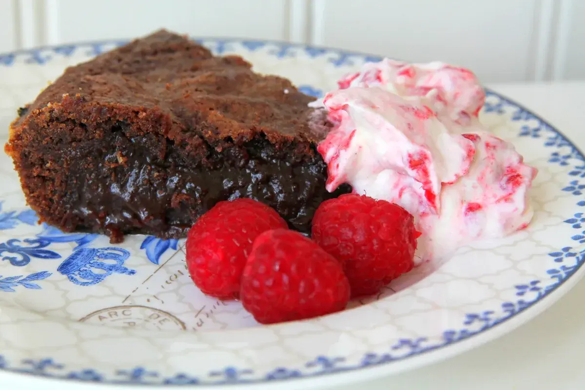 En bit kladdkaka med lakrits, serverad med hallon och grädde.