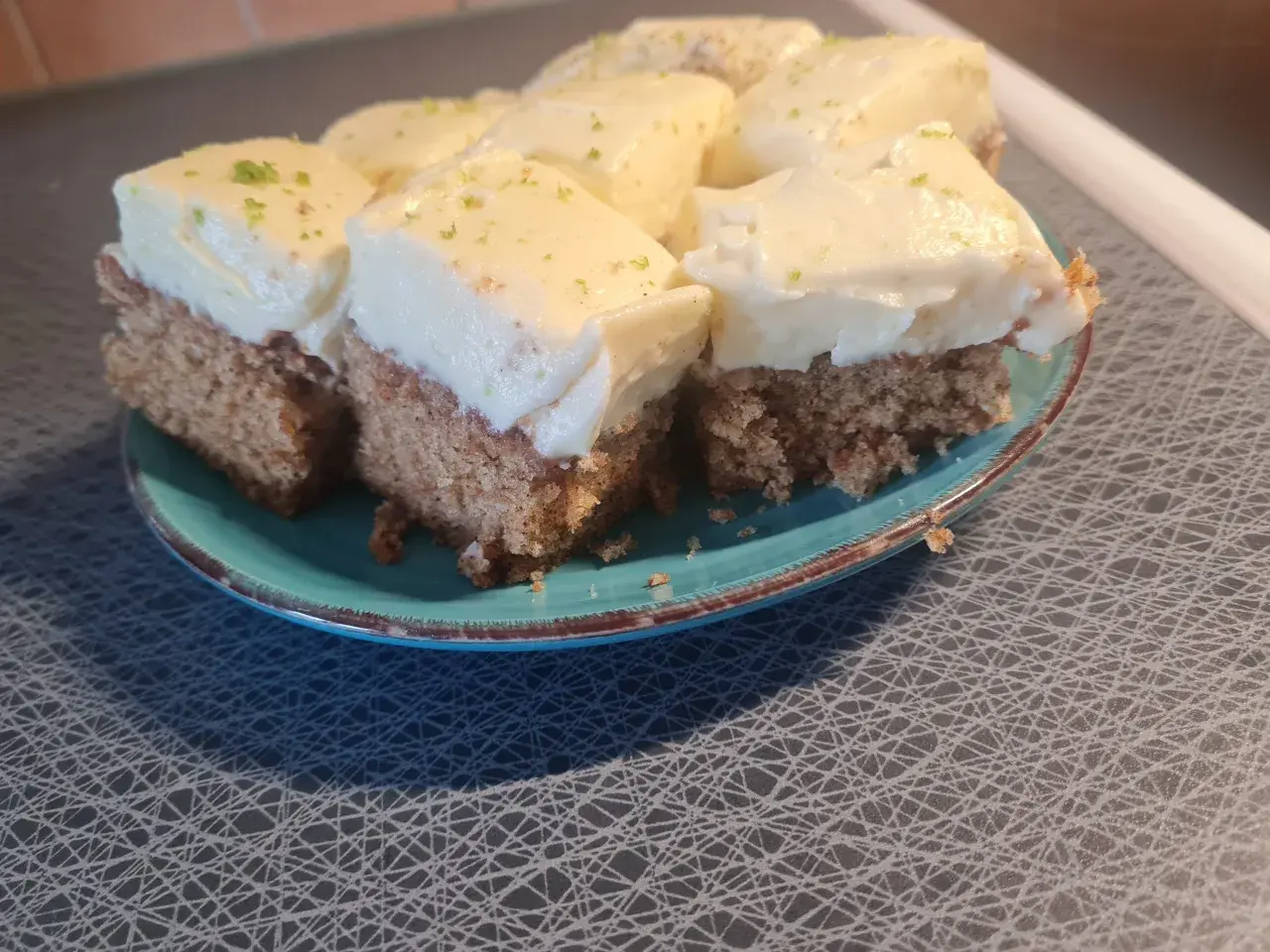 Sju bitar morotskaka med vit frosting och rivet citronskal på en turkos tallrik. Bra att veta att man kan frysa in morotskaka för senare njutning.