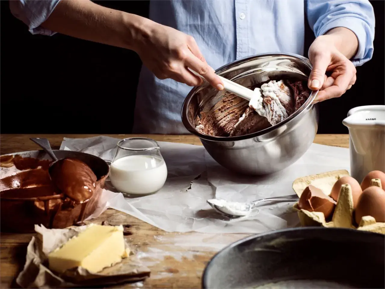 Händer blandar chokladsmet i skål. Ingredienser som smör, ägg och mjölkfri filmjölk ligger framme.