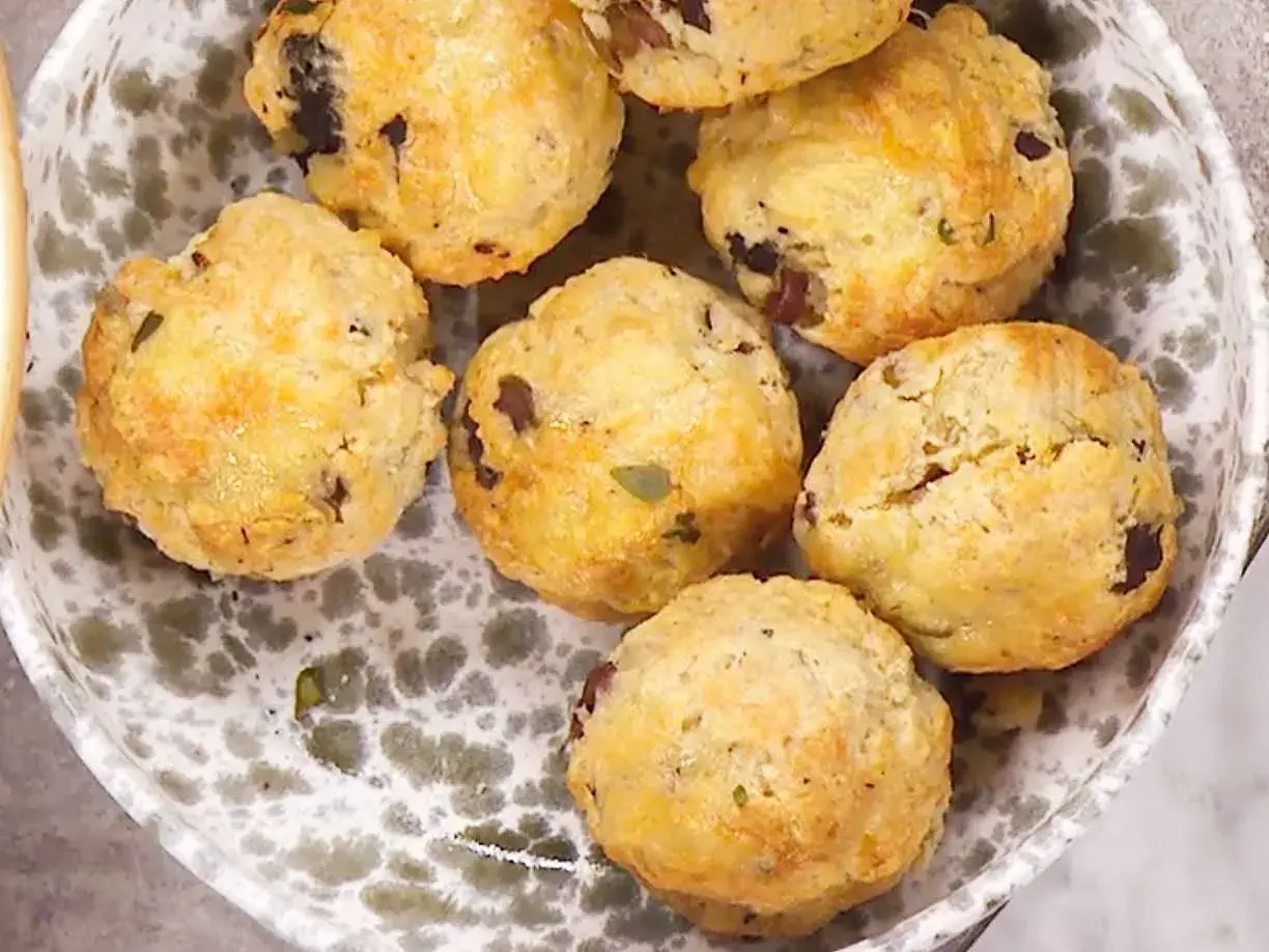 En skål med matiga scones, gyllene och med mörka bitar av oliver eller soltorkade tomater. Perfekta för en rejäl fika.
