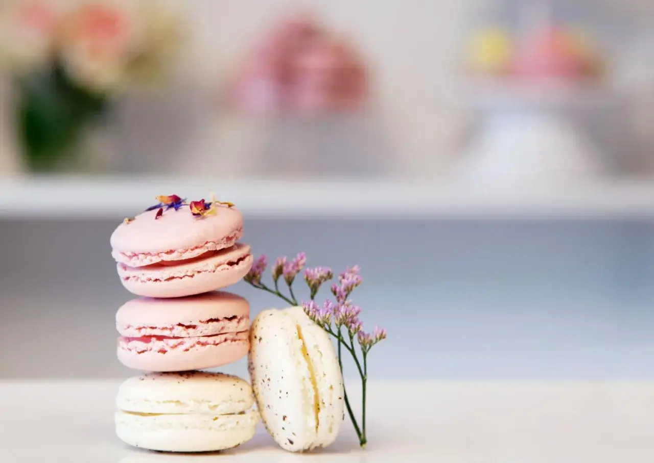 En stapel rosa och vita macarons, dekorerade med blomblad. Ett enkelt macarons recept för en vacker dessert.