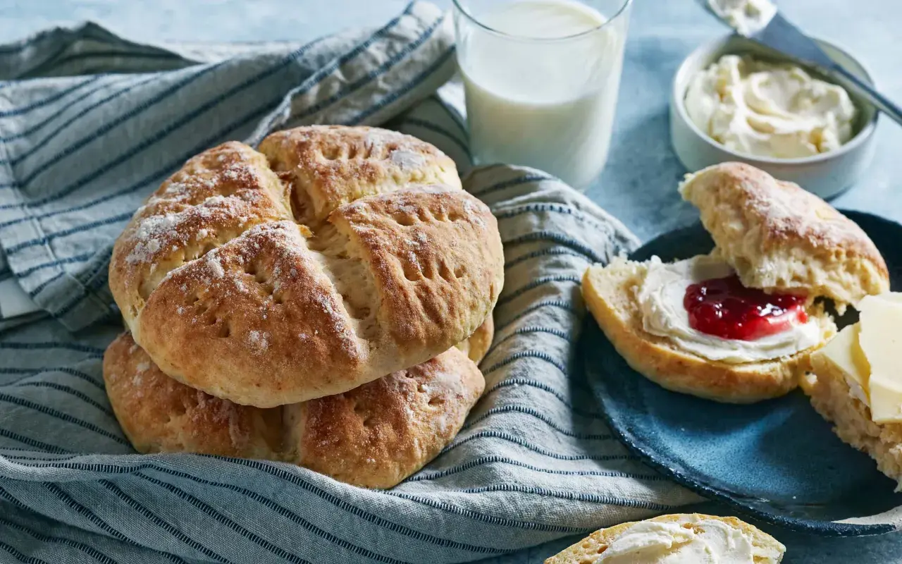 En hög med söta scones, redo att avnjutas med sylt och grädde. Ett glas mjölk står bredvid, perfekt för en mysig fika.