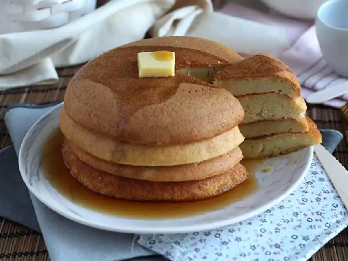 En hög med fluffiga japanska pannkakor, toppad med smör och sirap, serveras på en tallrik.
