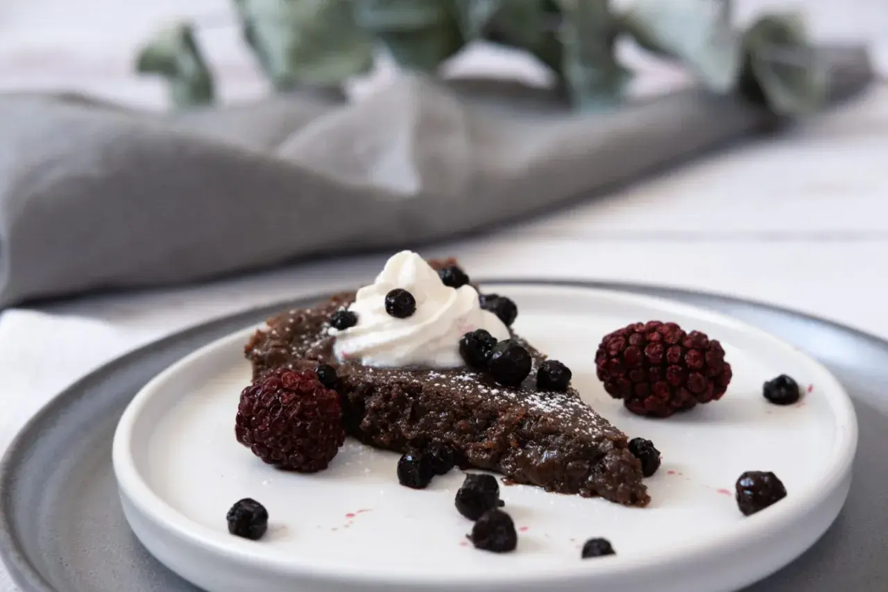 En bit vegansk kladdkaka med vispgrädde och bär.