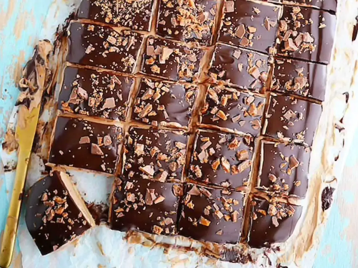 Biskvier i långpanna med chokladglasyr och krossad toffee. En gyllene kniv ligger bredvid.