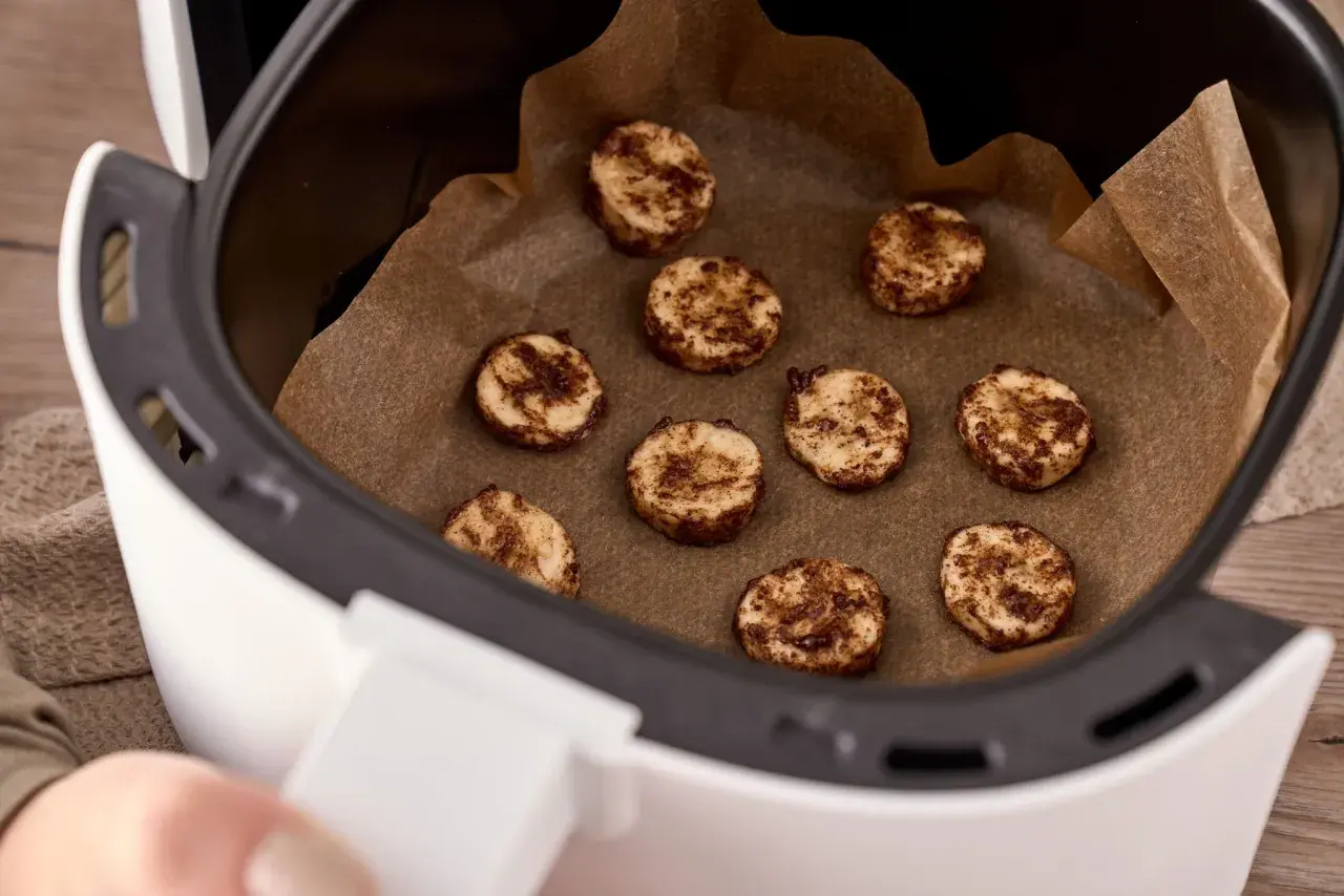 Små, runda kakor med kanel ligger på bakplåtspapper i en airfryer. Perfekt för att frysa in kakor för senare njutning.