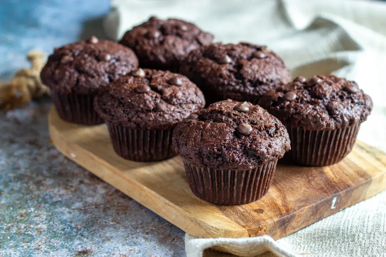 Fem amerikanska muffins med chokladbitar på en träbricka.