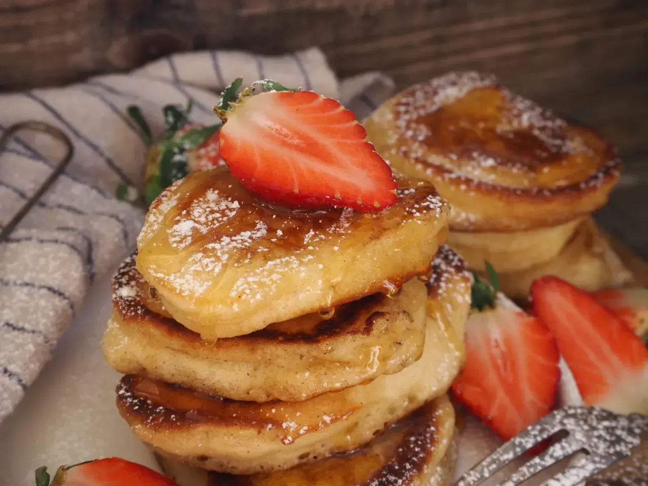 En stapel fluffiga pannkakor på filmjölk, toppade med färska jordgubbar och pudersocker.