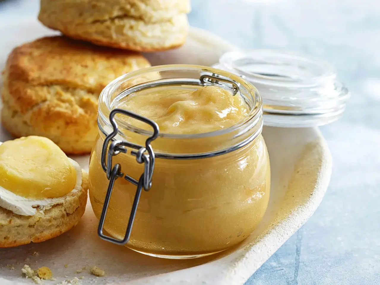 En burk med gyllene lemoncurd står bredvid scones. Ett perfekt recept för en härlig fika.