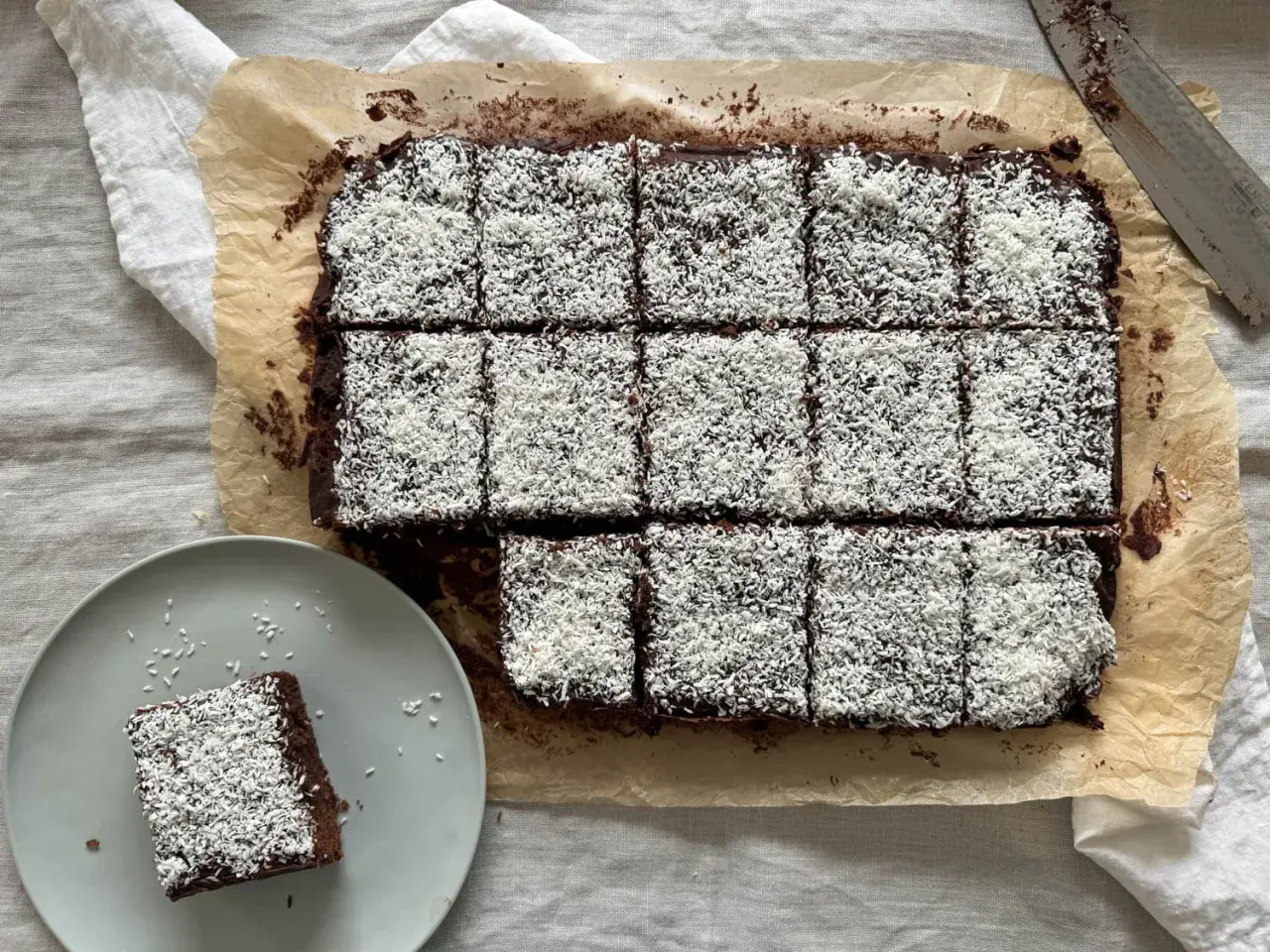 En plåt med chokladkakor, toppade med kokosflingor, redo att avnjutas som kärleksmums på påsk. En bit ligger på en tallrik.