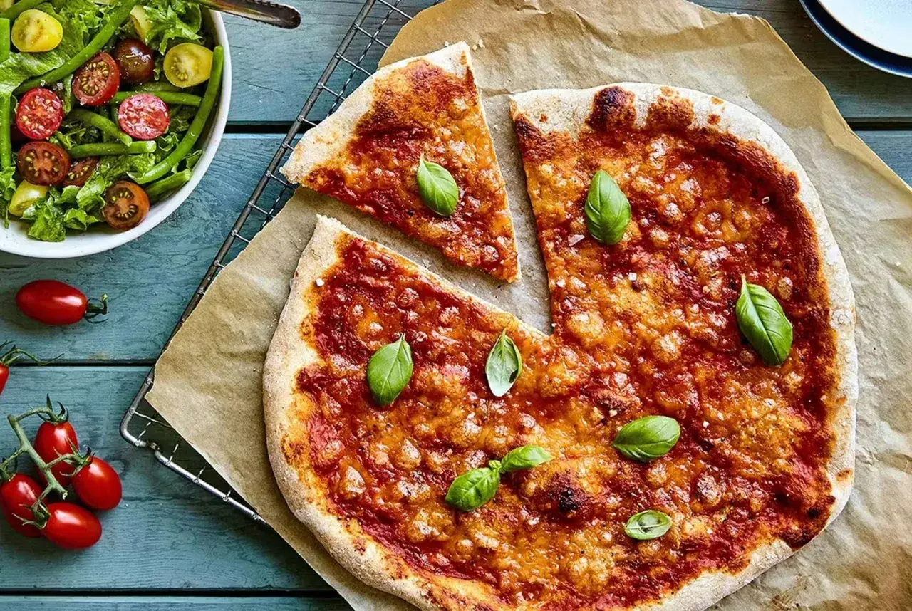 En hemmagjord pizza med nyttig pizzabotten, toppad med tomatsås och basilika. Bredvid en fräsch sallad med gröna bönor och tomater.