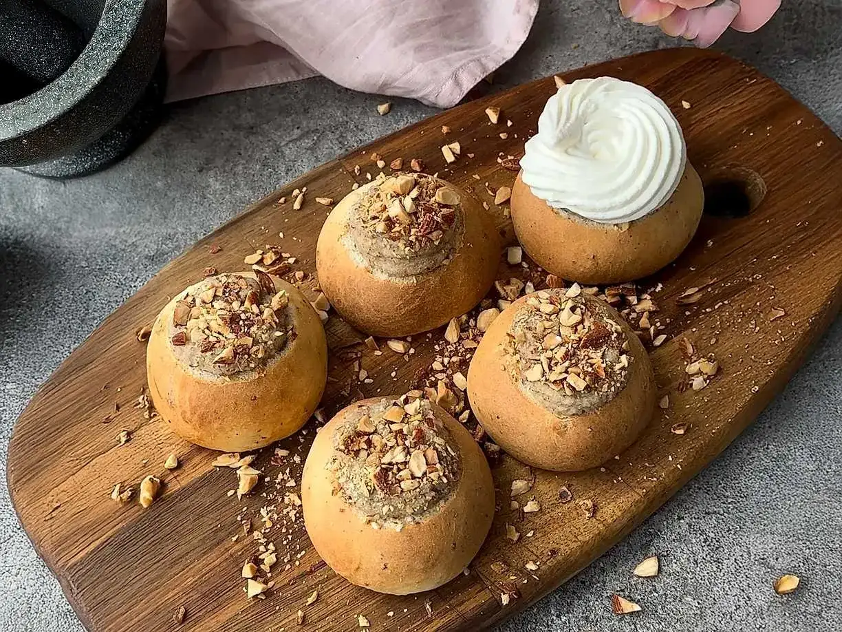 Färdiga semlor med mandelmassa till, toppade med hackade nötter och en generös klick grädde på en av dem.