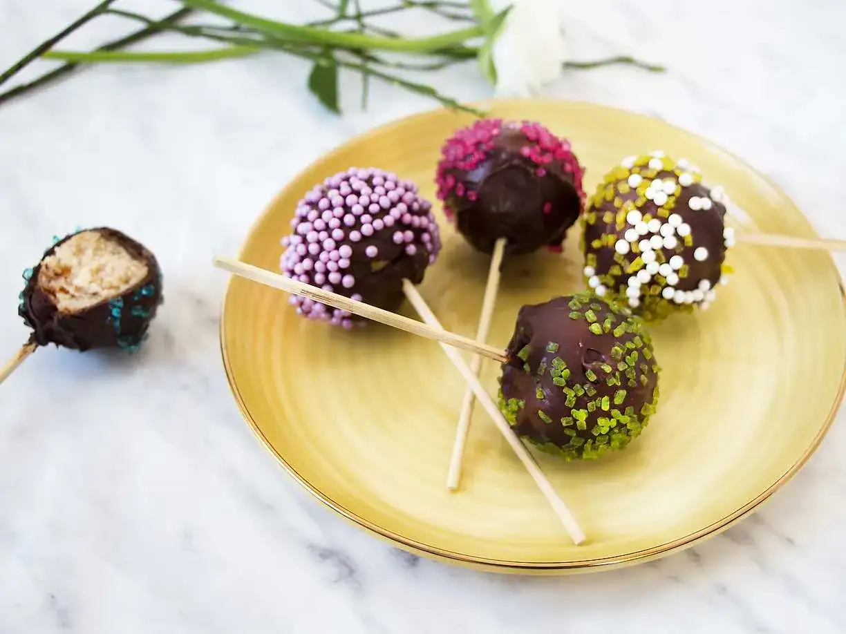 Fem chokladöverdragna cake pops med olika strössel ligger på en gul tallrik. En är uppäten.