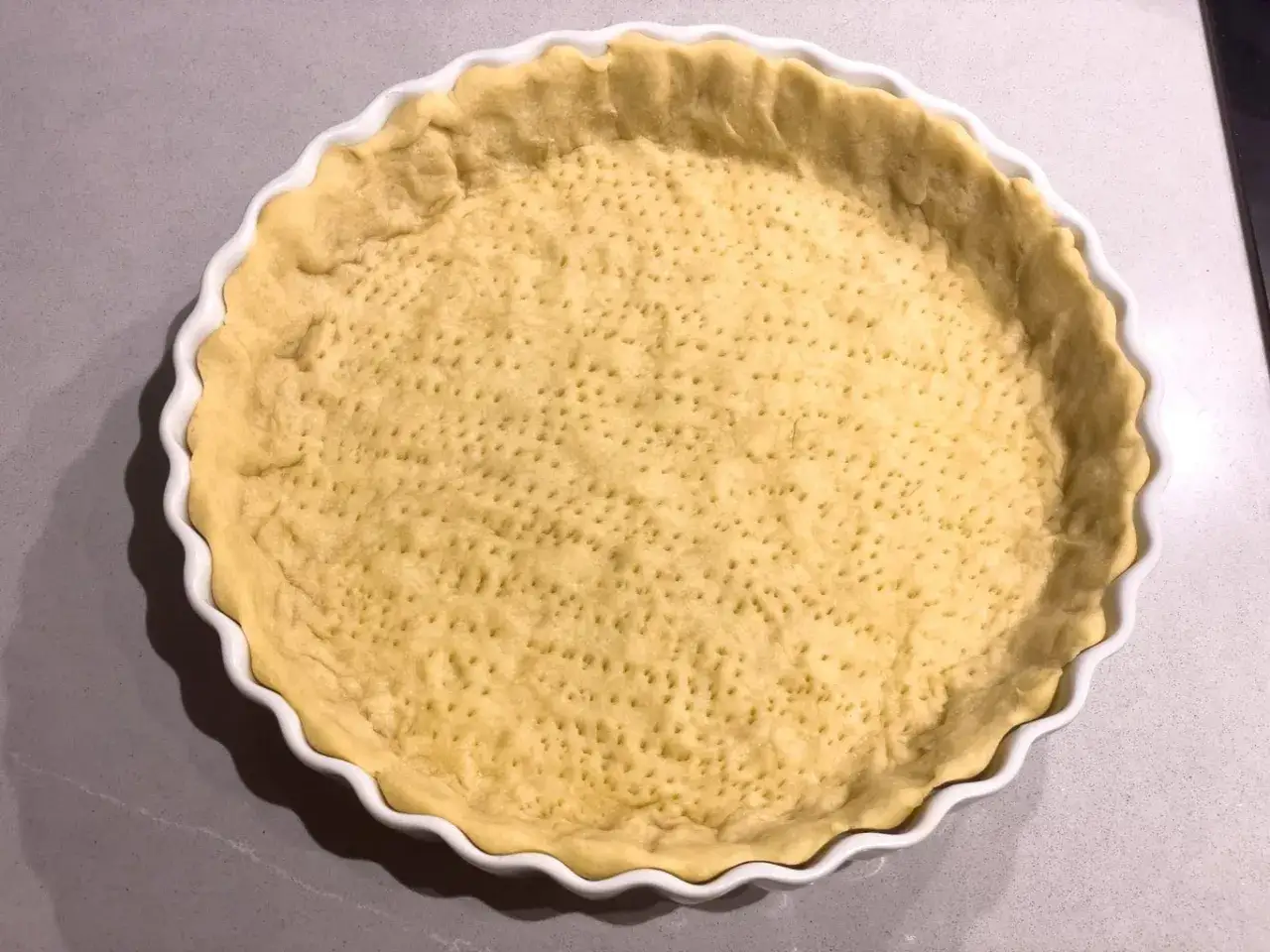 En färdiggjord pajdeg i en vit pajform, redo för fyllning. Perfekt för ditt pajdeg recept.
