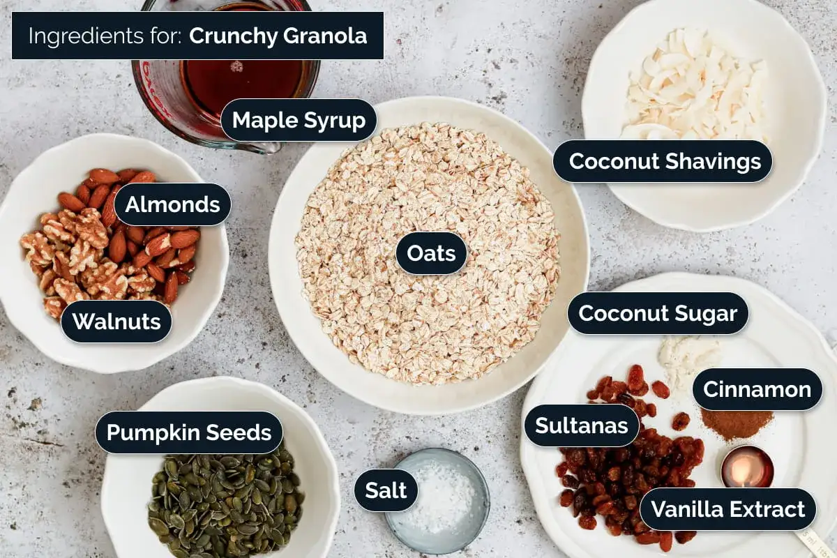 Ingredienser för ett krispigt granola recept: havre, mandlar, valnötter, pumpafrön, lönnsirap, kokosflingor, kokossocker, kanel, russin, vaniljextrakt och salt.
