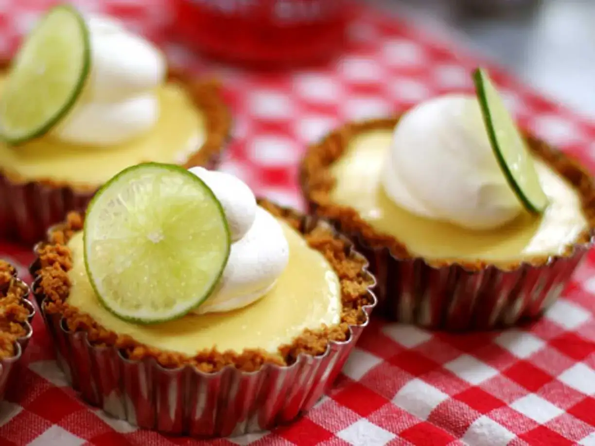 Små key lime pies med vispad grädde och limeklyfta, serverade på en rödvitrutig duk.