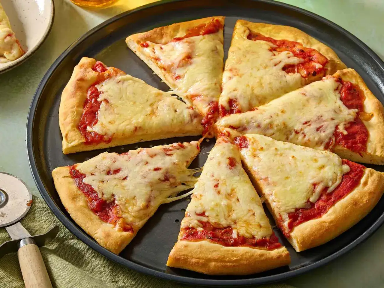 En hel pizza med tomatsås och smält ost, skuren i åtta bitar. En nyttig pizzabotten som ser gyllene och inbjudande ut.