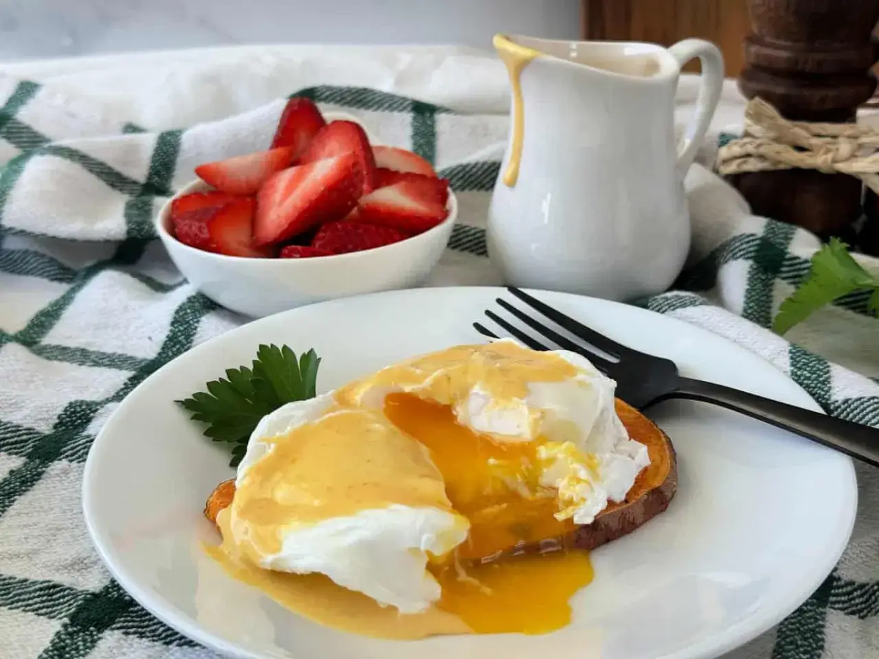 En perfekt frukost med eggs benedict på en sötpotatisbotten, serverad med färska jordgubbar och en liten kanna hollandaisesås.