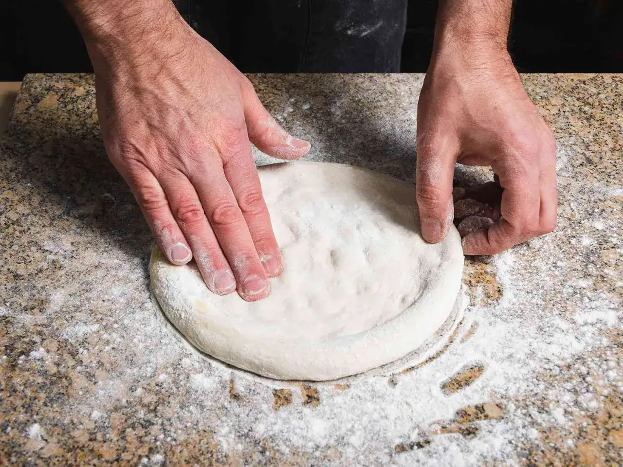 Händer formar pizzadeg på ett mjölat stenbord. Ett perfekt pizzadeg recept börjar här.