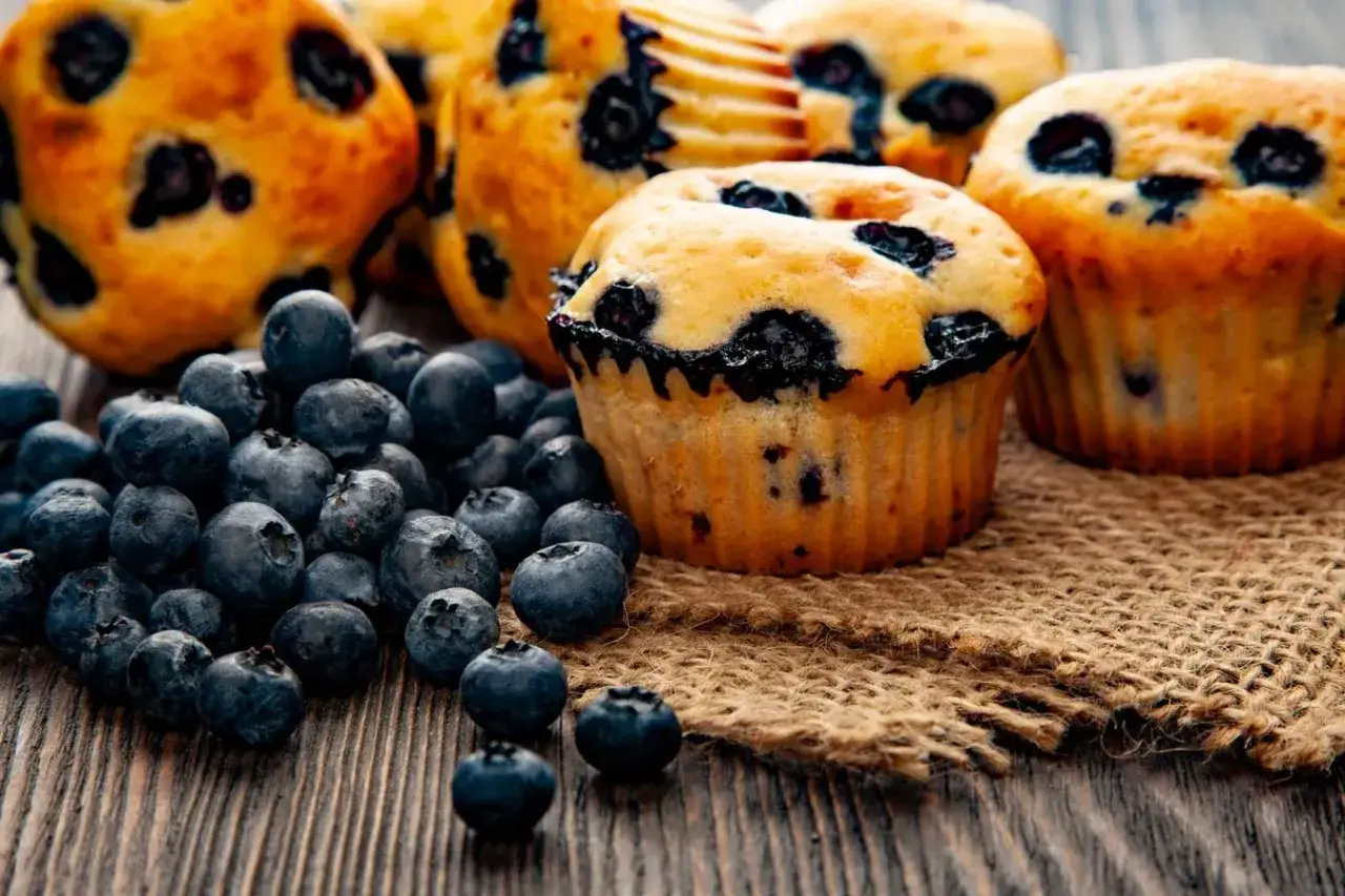 Amerikanska muffins med blåbär, redo att avnjutas. En hög med färska blåbär ligger bredvid de gyllene bakverken.