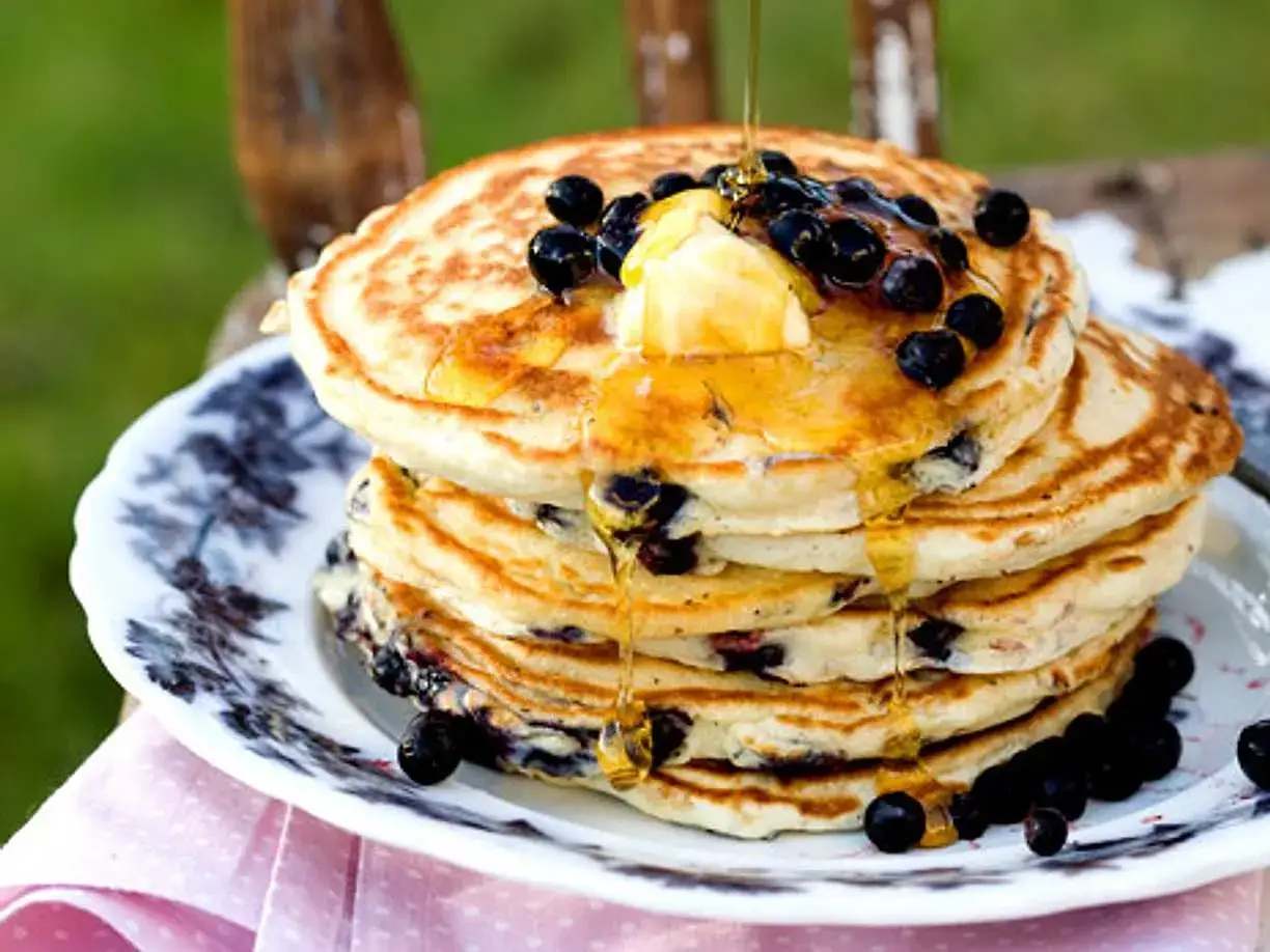 En hög med fluffiga american pancakes med blåbär, smör och sirap som rinner ner. En härlig frukost!
