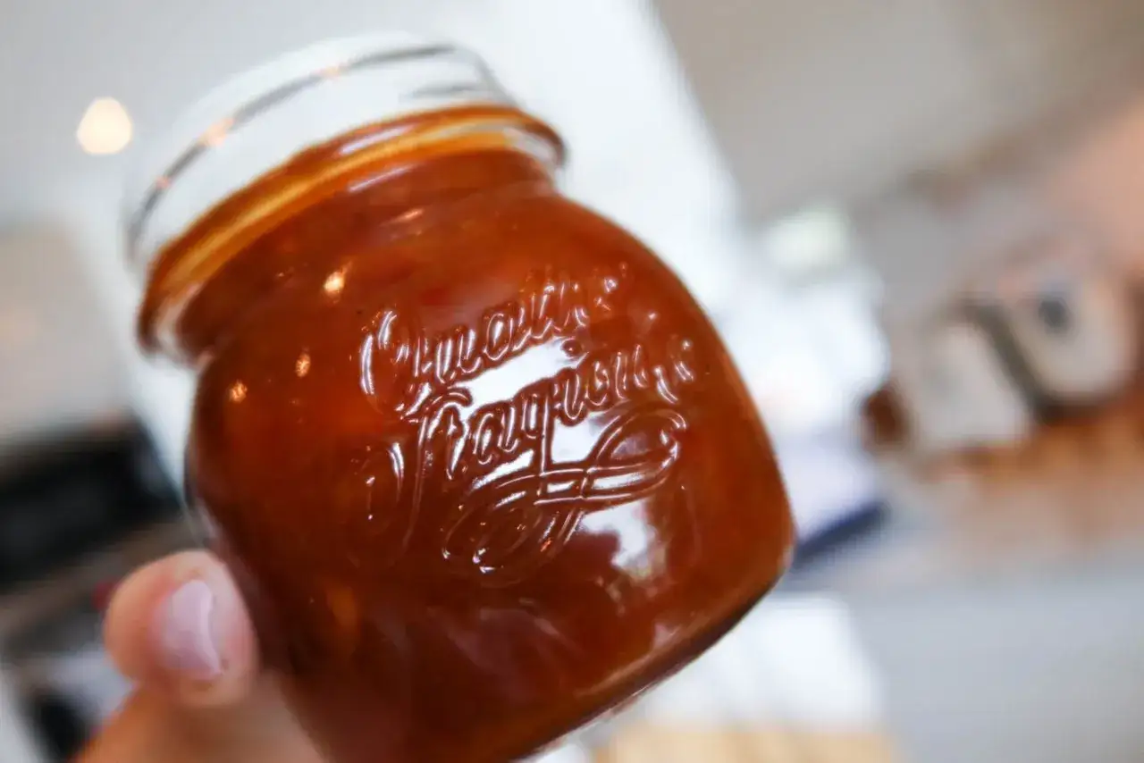 En hand håller ett glas med en härlig rabarber chutney. Den glansiga ytan reflekterar ljuset.