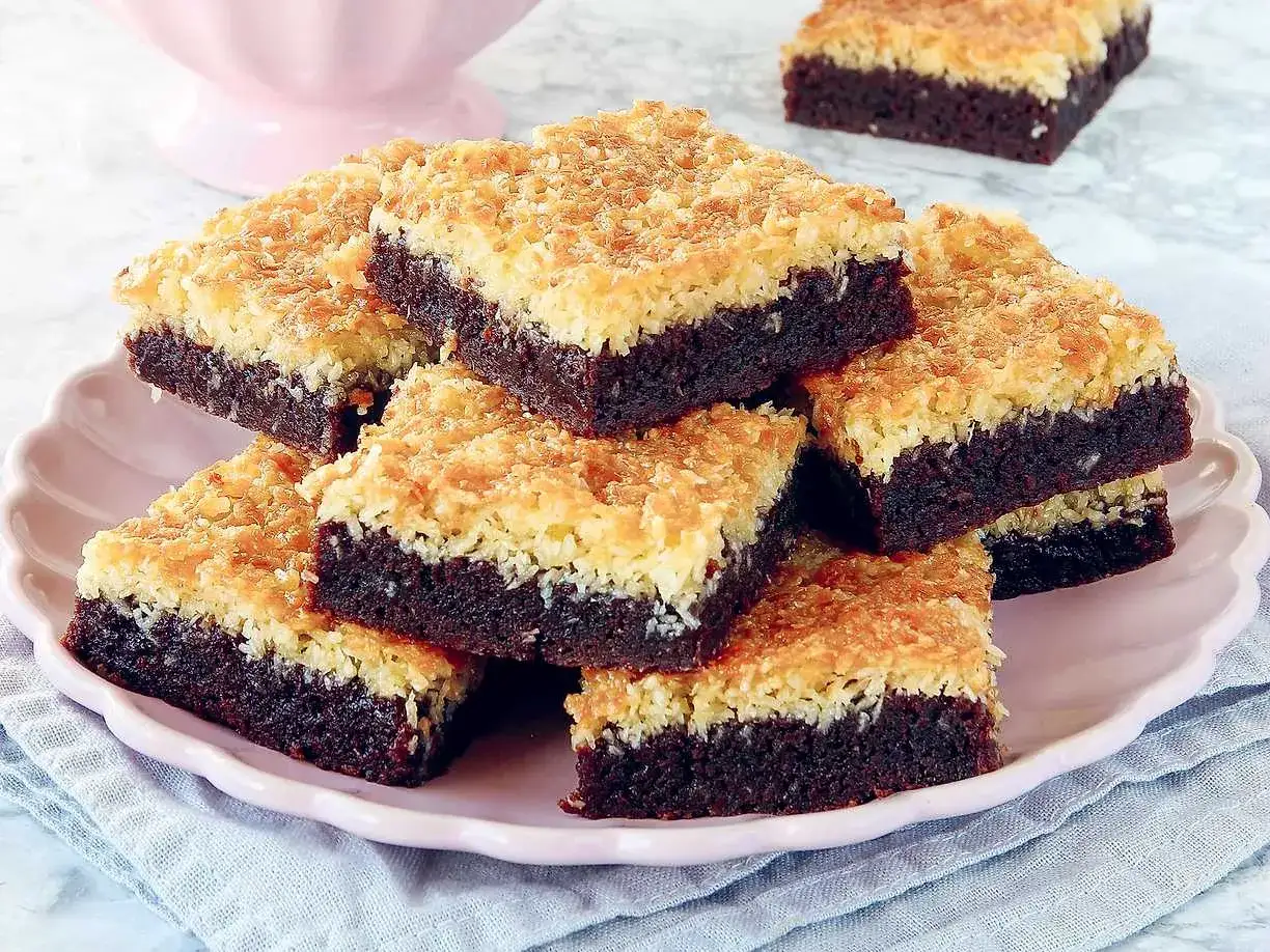 En hög med kladdkaka med kokostosca på en rosa tallrik. Den mörka chokladbottnen toppas av en gyllene, krispig kokosgrädde.