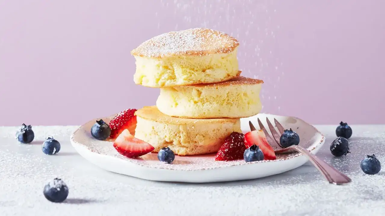 Fluffiga japanska pannkakor staplade högt, pudrade med florsocker och serverade med färska bär.
