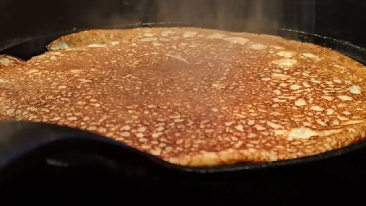 En gyllene, nygräddad pannkaka steker i en stekpanna. Perfekt för en mysig frukost med glutenfria pannkakor.