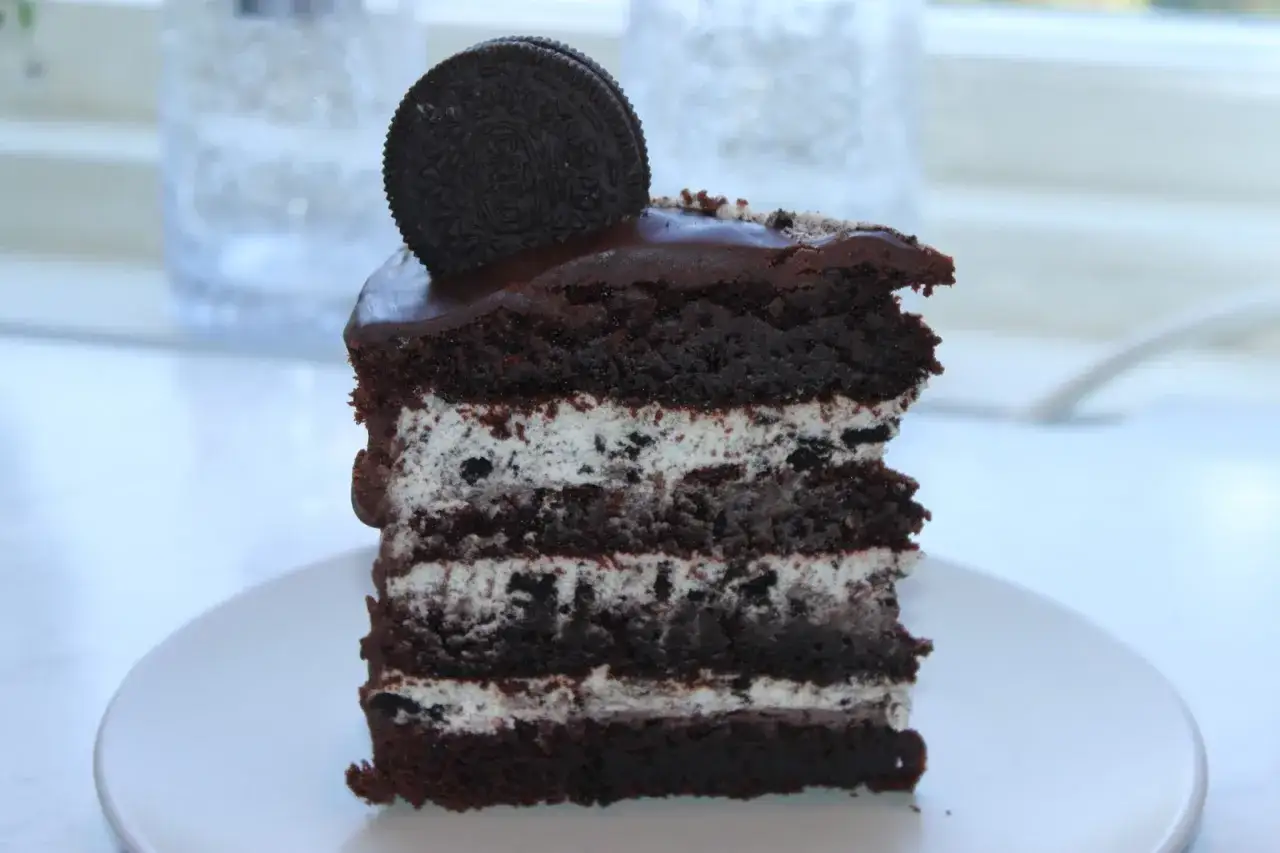 En bit chokladkaka med lager av krämig fyllning och krossade oreos. En hel oreo vilar på toppen av denna läckra oreo tårta.