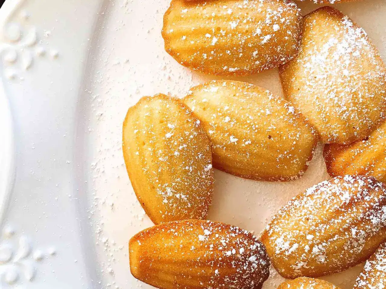 En tallrik med gyllene madeleinekakor, pudrade med florsocker, perfekta för afternoon tea.