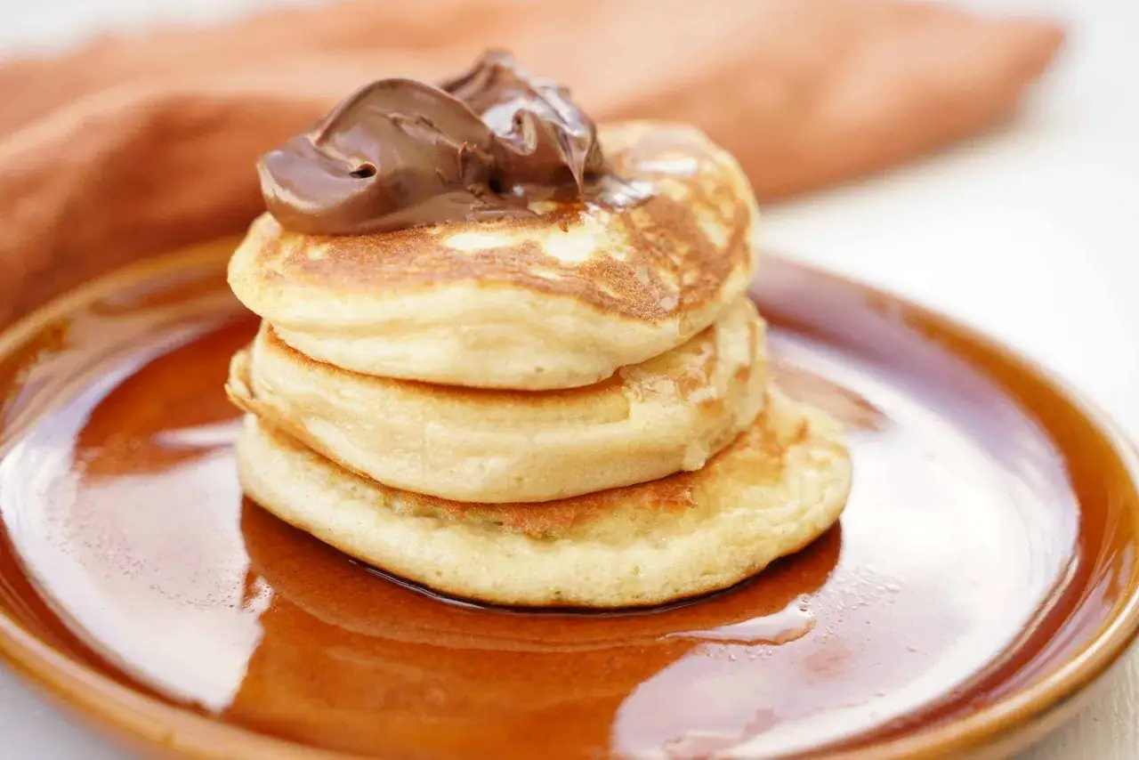 En stapel fluffiga pannkakor på filmjölk toppas med chokladkräm på en brun tallrik.